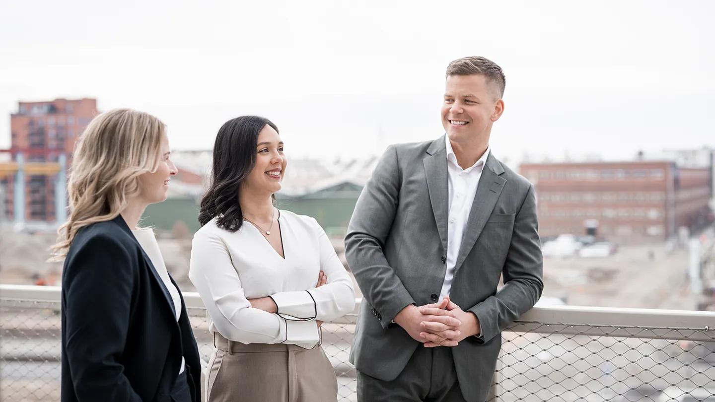Två kvinnor och en man i kostym står utomhus och pratar